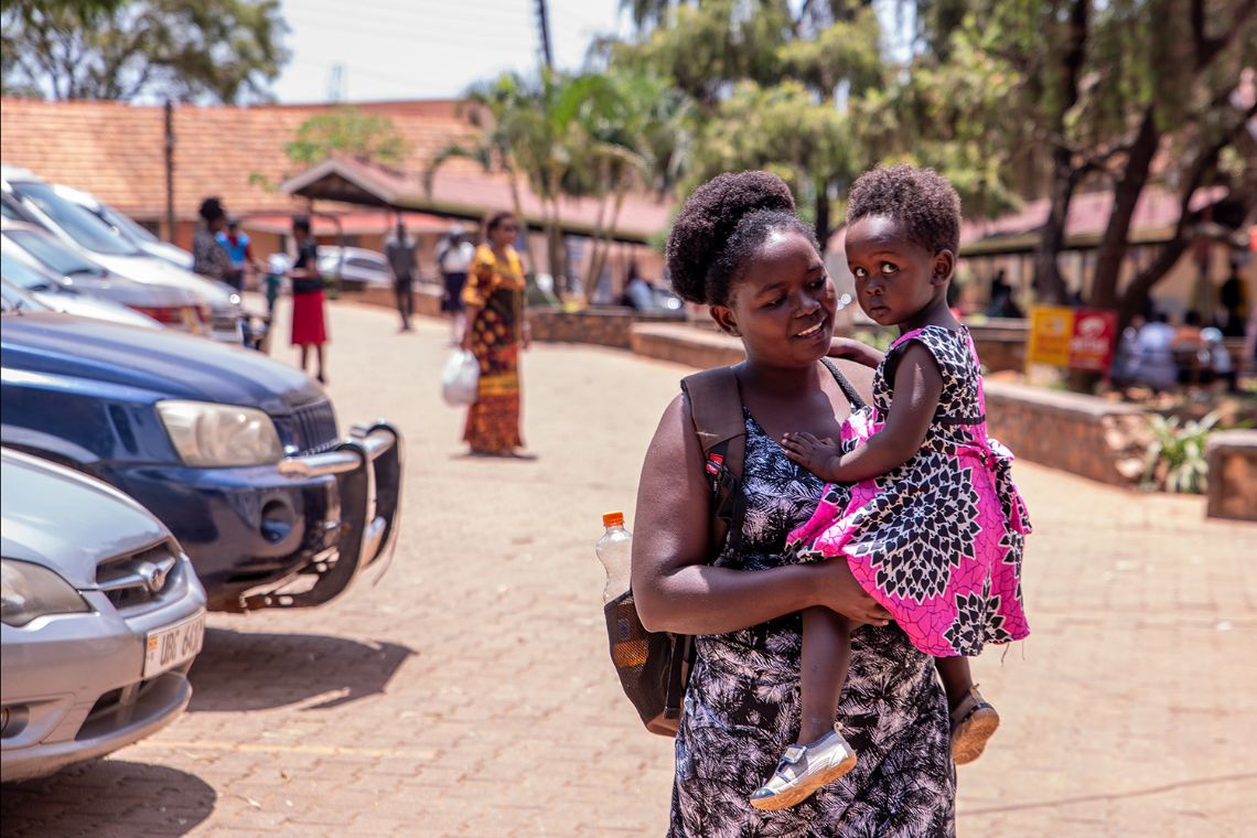 Eine Frau geht mit einem kleinen Mädchen auf dem Arm über einen Parkplatz.