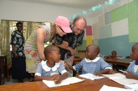 Eine Frau und ein Mann beugen sich zu zwei Schulkindern, die an einem Schreibtisch im Klassenzimmer sitzen.