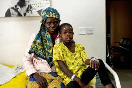 Eine Frau und ein Mädchen sitzen auf einem Krankenhausbett. Das Kind hat Markierungspflastern auf der Stirn über beiden Augen.