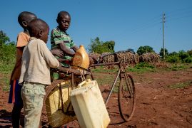 Drei kleine Jungen beladen ein Fahrrad mit Wasserkanistern aus Plastik.