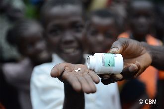 Ein afrikanisches Kind streckt seine Handfläche hin, jemand gibt zwei Tabletten darauf.