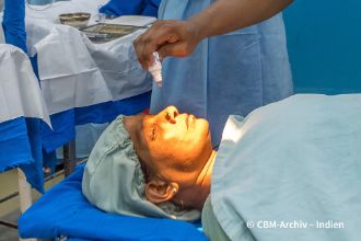 Graue-Star-Operation Kosten – Eine Frau in OP-Hemd bekommt auf dem OP-Tisch Augentropfen.