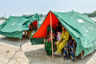 In zwei Schutzzelten sitzen Menschen in bunter Kleidung.