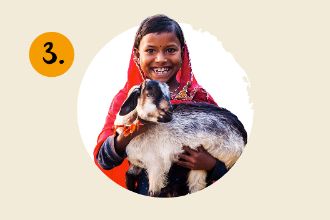 Ein Mädchen im roten Sari hält eine Ziege in den Armen.