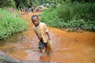 Ein kleiner Junge schleppt einen vollen Wasserkanister durch einen seichten Fluss. Foto: CBM