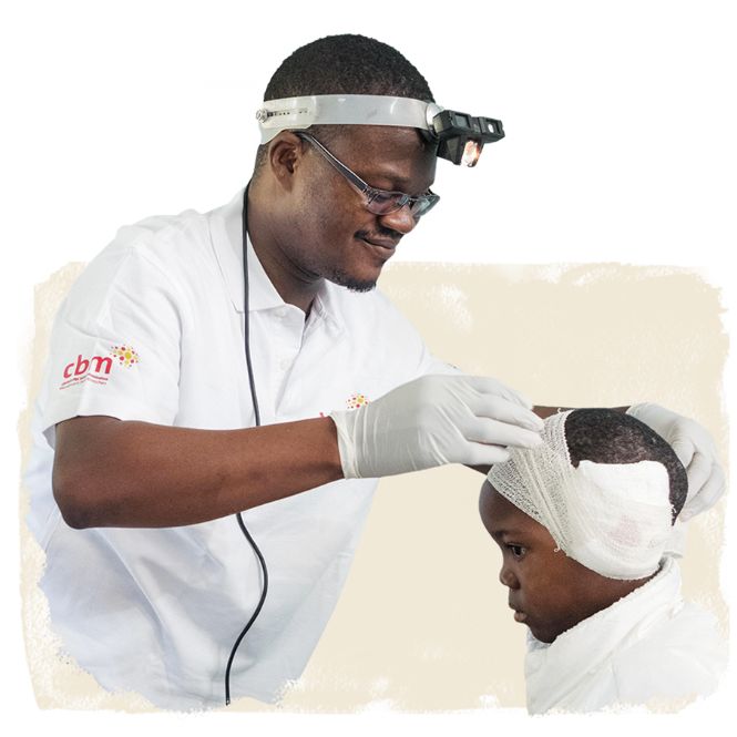 Ein Mann entfernt nach Spenden-Geschenk Ohrenoperation den Kopfverband eines Kindes.