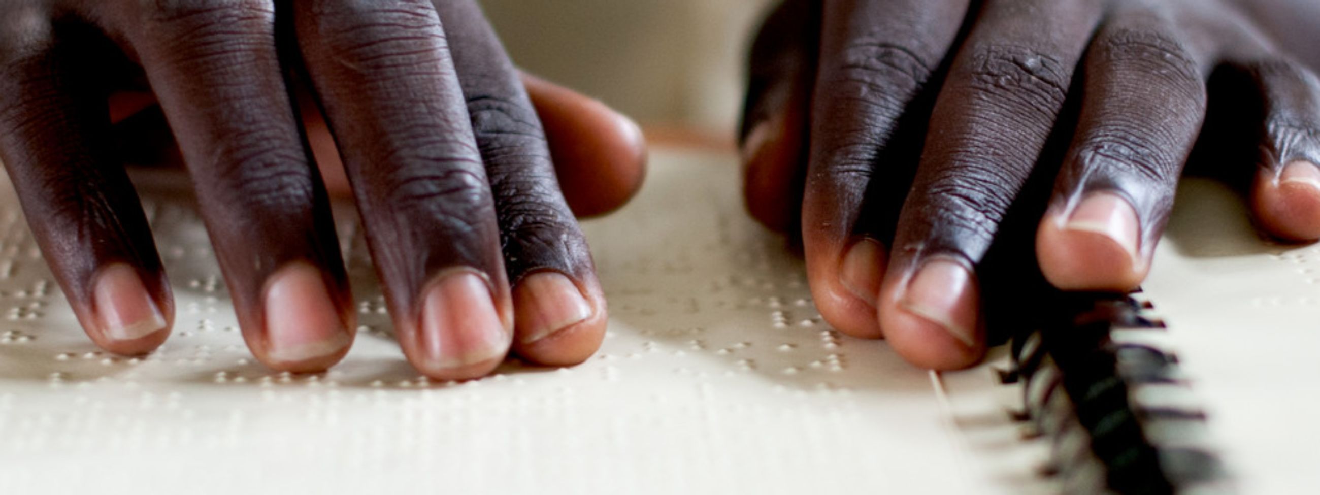 Zwei Hände fahren über ein aufgeschlagenes Heft mit Blindenschrift.