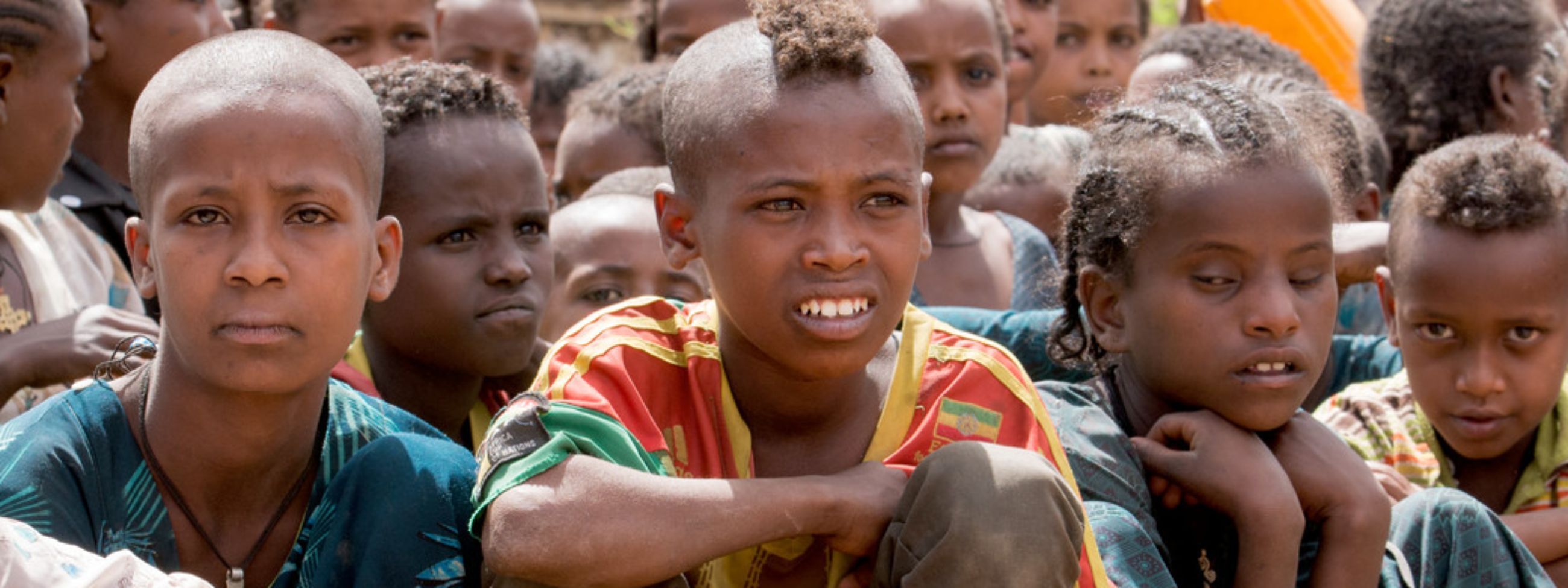 Mehre Kinder hocken mit Wasserkanistern am Boden.