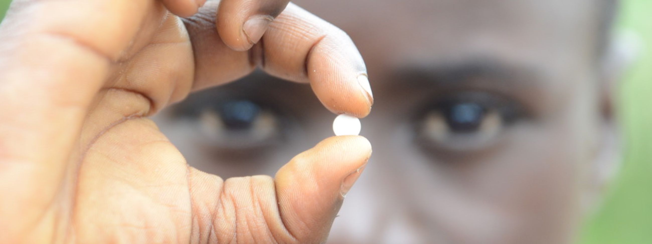 Ein afrikanisher Junge hält eine kleine Tablette zwischen den Fingern und hält sie vor sein Gesicht.