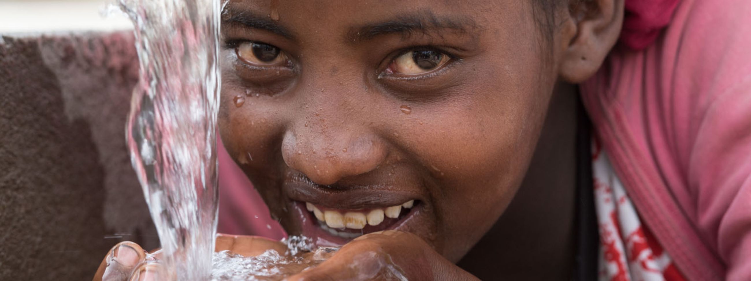 Ein Mädchen trinkt Wasser aus einem Brunnen.