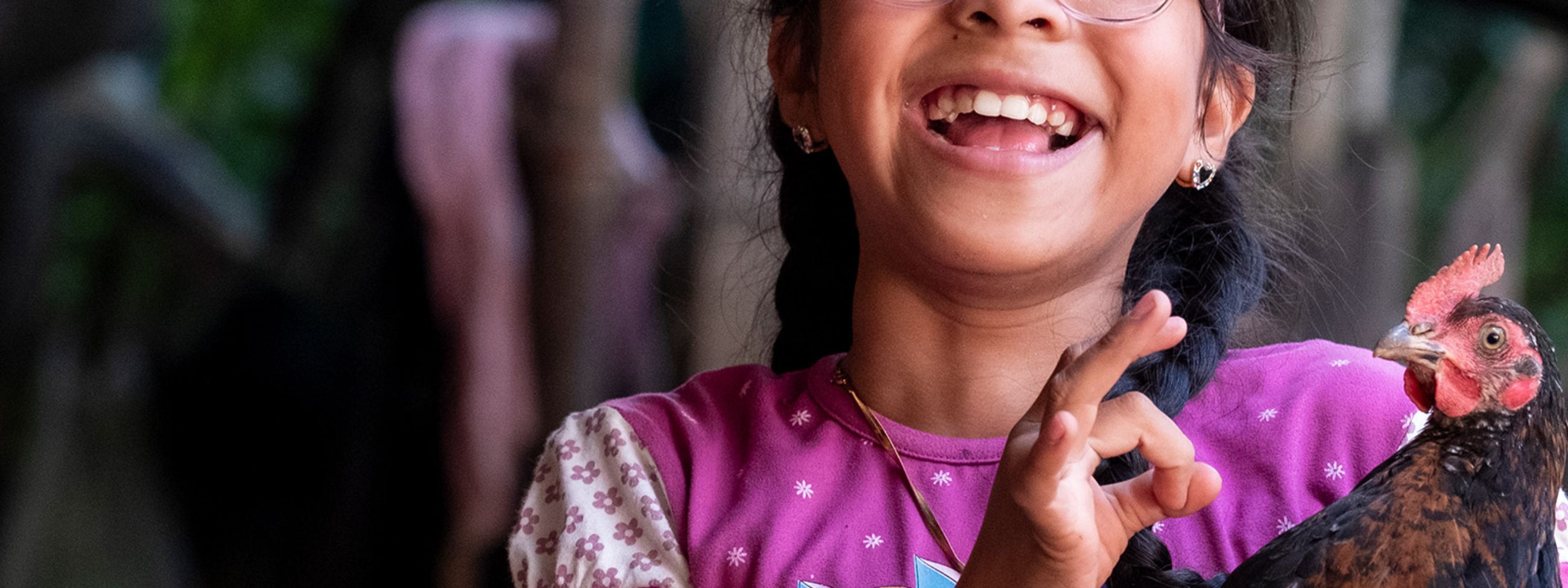 Ein Mädchen mit Zöpfen hält ein Huhn im Arm.