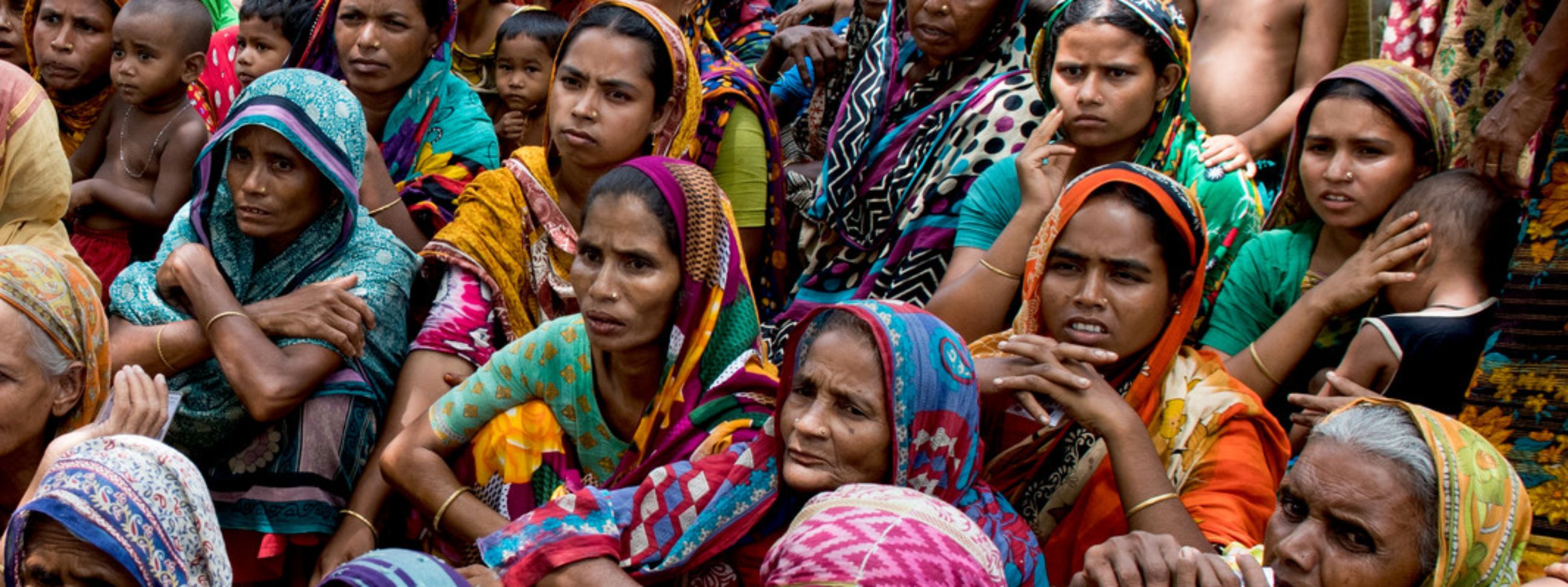 Eine große Gruppe bunt gekleideter asiatischer Frauen hockt am Boden.