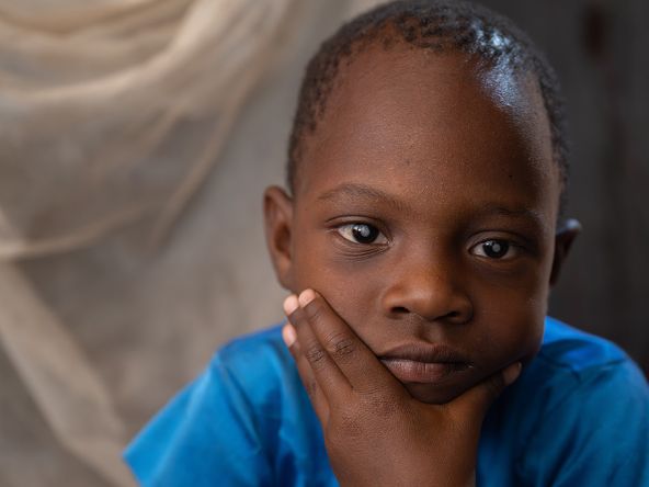 Ein etwa fünfjähriges Mädchen mit weißen Pupillen hat das Kinn auf die Hand gestützt.
