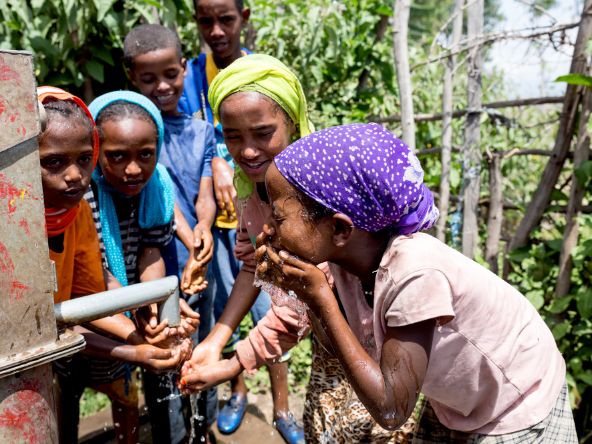 Afrikanische Schüler*innen waschen sich an einer Wasserpumpe das Gesicht