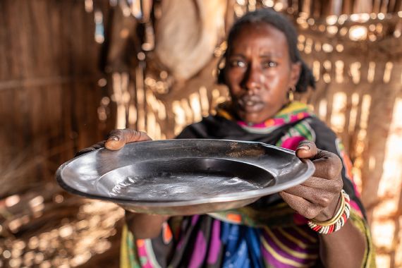 Eine Frau in bunter Massai-Kleidung hält einen leeren Teller hoch.