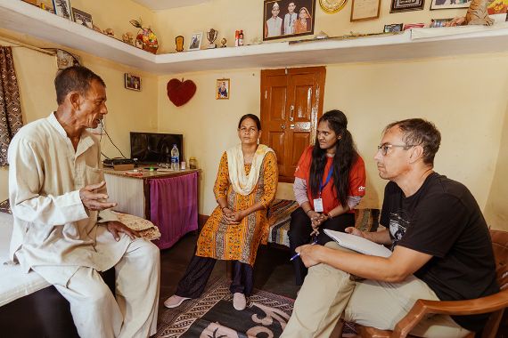 Zwei Männer und zwei Frauen sitzen in einem Wohnraum in einer Runde. Der ältere Mann spricht, die anderen hören zu.