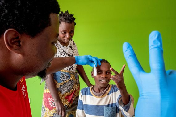 Ein Mann hält zwei Finger hoch, der Junge, dessen Augenverband gerade entfernt wird, macht es nach.