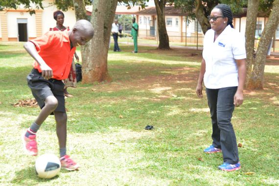 Ein Junge spielt Fußball, während die Phyiotherapeutin zusieht