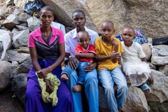 Eine Frau in buntem Kleid, ein Junge im Teenager-Alter und drei kleinere Kinder sitzen auf Felsbrocken.