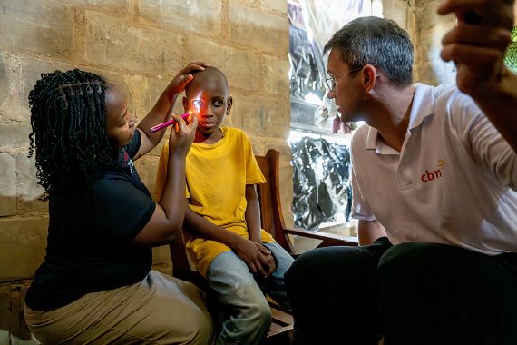 Eine Frau leuchtet mit einer Handlampe in die Augen eines etwa zehnjährigen Jungen, ein Mann hält eine Hand hoch.