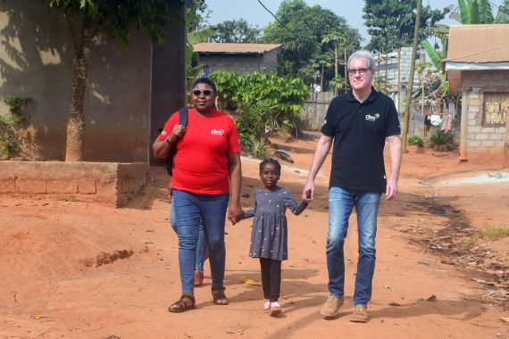 Eine Frau, ein kleines Mädchen und ein Mann gehen nebeneinander. Die Erwachsenen führen das Kind in ihrer Mitte an der Hand.