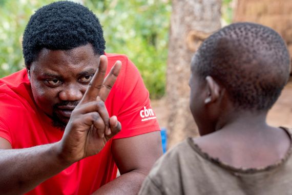 Ein Mann hält für einen Sehtest Mittel- und Zeigefinger vor das Gesicht eines Kindes.