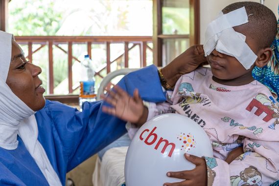 Eine Frau fasst an den Augenverband eines kleinen Jungen.