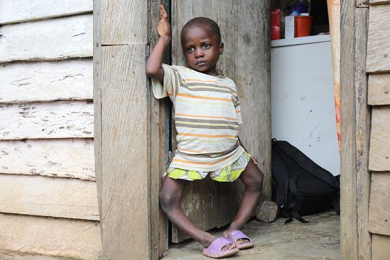 Ein etwa fünfjähriges Mädchen steht im Türrahmen einer Holzhütte.