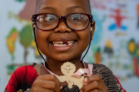 Ein kleines Mädchen mit Brille hält einen kleinen Holzengel in den Händen.
