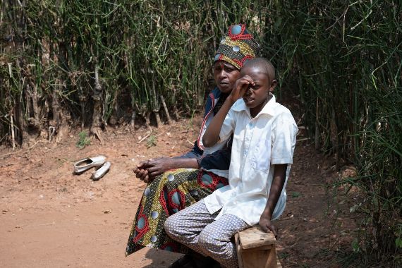 Ein etwa 13-jähriger Junge sitzt mit einer Frau auf einer kleinen Holzbank.