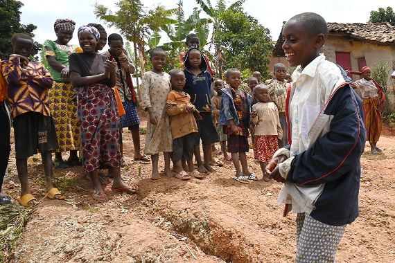 Ein etwa 13-jähriger Junge geht lachend an einer Gruppe von Menschen vorbei und einer Hütte vorbei.