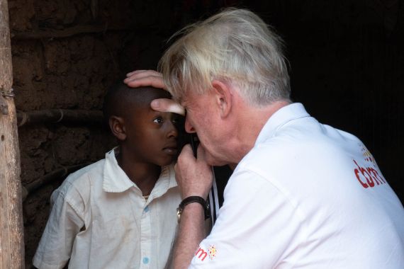 Ein Mann schaut mit einer Handlupe in die Augen eines etwa elfjährigen Jungen.
