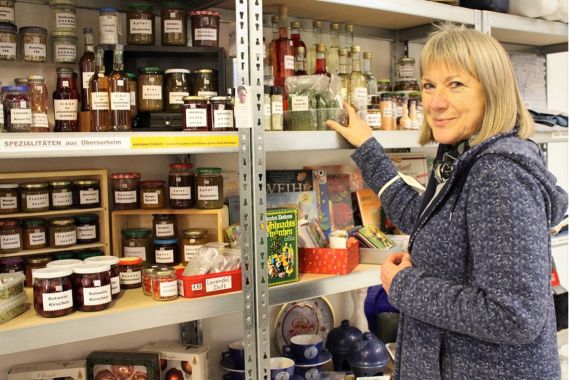 Eine Frau steht vor einem Regal mit Marmeladen, Sirups sowie anderen Lebensmitteln in Gläsern.