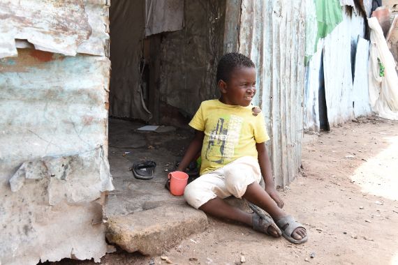 Ein etwa siebenjähriger Junge sitzt auf der Türschwelle einer Hütte.