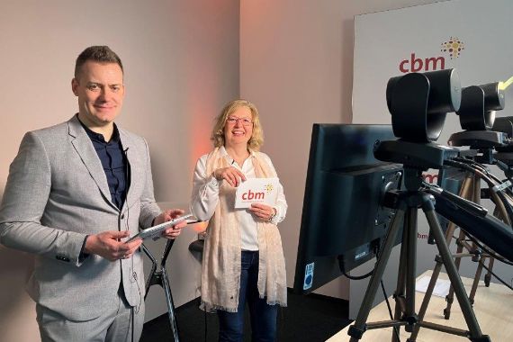 Ein Mann und eine Frau halten Notizkarten in den Händen, vor ihnen stehen mehrere Monitore auf Ständern.