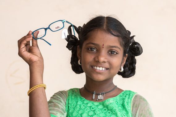 Mädchen hält lächelnd eine neue Brille hoch
