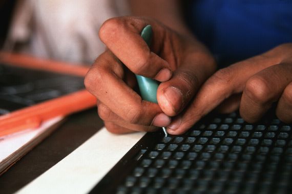 Zwei Hände halten einen Griffel und schreiben Braille.