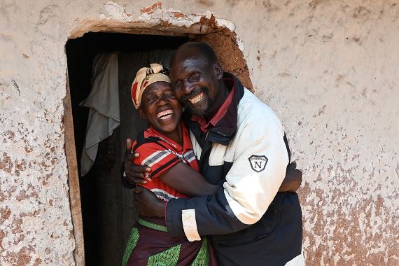 Eine Frau und ein Mann, beide um die 60, umarmen sich lachend.