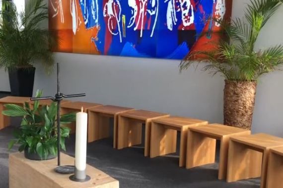 Andachtsraum mit Kreuz, Kerze und buntem Glasbild