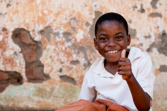 Ein afrikansicher Junge sitzt auf einer Stufe und hebt lachend den Daumen in die Luft.