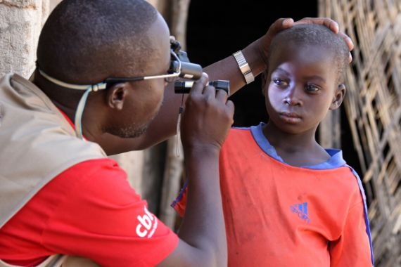 Ein Mann leuchtet einem etwa 10-jährigen Junge mit einer kleinen Lampe ins rechte Auge.