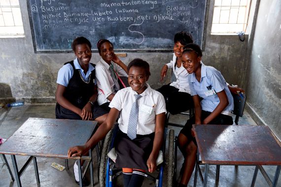 Ein Mädchen im Rollstuhl sitzt mit anderen Mädchen in einem Klassenzimmer.