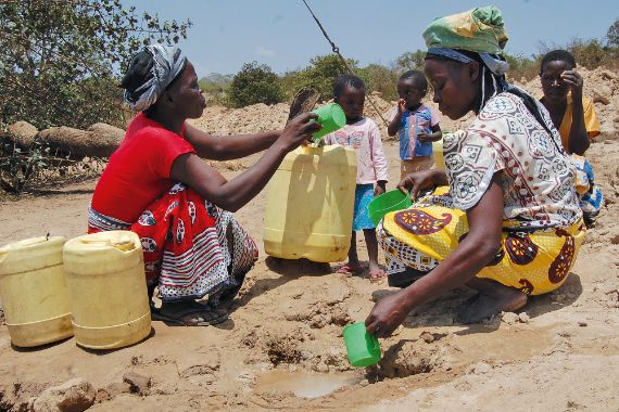 Zwei afrikanische Frauen schöpfen Wasser aus einer Pfütze und füllen es in Kanister.