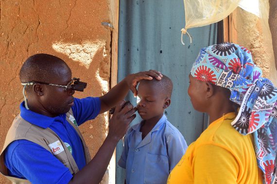 Ein Mann untersucht mit Hilfe einer Handlampe die Augen eines Jungen, eine Frau schaut zu.