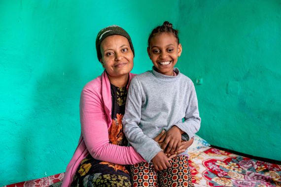 Ein Mädchen (r.) sitzt auf dem Schoß einer Frau.