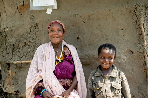 Eine Frau und ein Junge sitzen lächelnd vor einer Lehmwand.