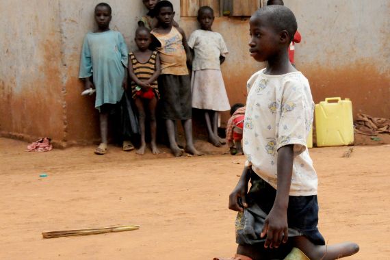 Ein Mädchen ohne Füße steht mit den Knien auf Badeschuhen. Im Hintergrund stehen mehrere andere Kinder und beobachten sie. 