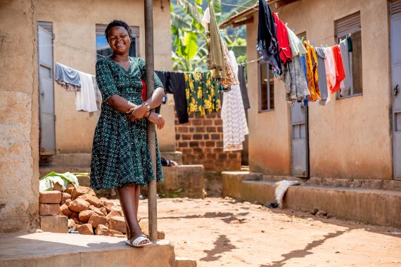 Eine Frau steht an einem Pfoten gelehnt in einem Hof zwischen Lehmhäusern.
