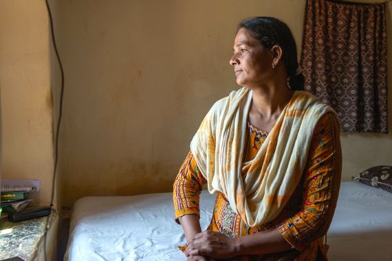 Eine Frau im Sari sitzt auf einem Bett und schaut in Richtung einer Fensternische.