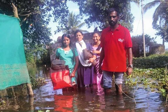 Überschwemmung: Drei Frauen und ein Mann waten durch kniehohes Wasser der Flut durch einen Monsunregen.